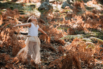 Little caucasian baby girl squatting in the forest among ferns