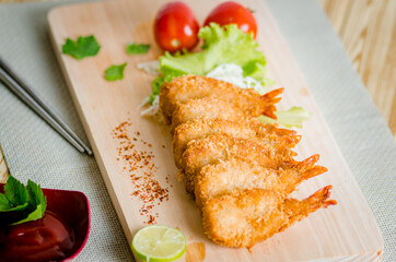Butterfly ebi furai shrimp served with tomato and lettuce on a wooden chopping board along with ketchup