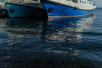 white blue ships boats bottoms on pier in bay of lake baikal with reflections in water  in light of...