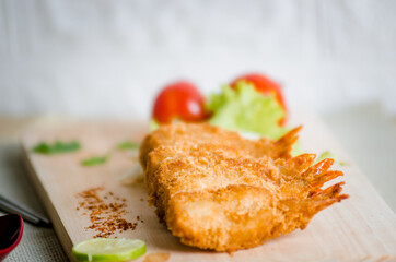 Butterfly ebi furai shrimp served with tomato and lettuce on a wooden chopping board along with ketchup