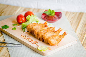 Butterfly ebi furai shrimp served with tomato and lettuce on a wooden chopping board along with ketchup
