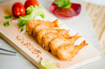 Butterfly ebi furai shrimp served with tomato and lettuce on a wooden chopping board along with ketchup