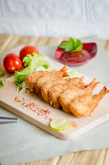 Butterfly ebi furai shrimp served with tomato and lettuce on a wooden chopping board along with ketchup
