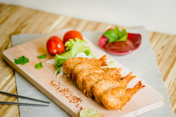 Butterfly ebi furai shrimp served with tomato and lettuce on a wooden chopping board along with ketchup