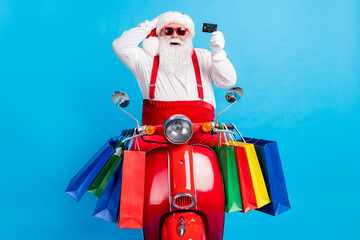 Excited white grey hair bearded stylish modern santa claus drive x-mas christmas motor bike hold credit card season tradition sale wear red suspenders overall isolated blue color background