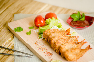 Butterfly ebi furai shrimp served with tomato and lettuce on a wooden chopping board along with ketchup