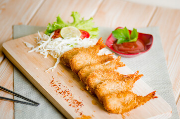 Butterfly ebi furai shrimp served with tomato and lettuce on a wooden chopping board along with ketchup