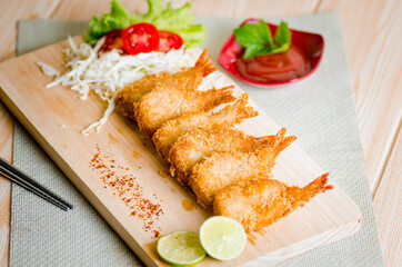 Butterfly ebi furai shrimp served with tomato and lettuce on a wooden chopping board along with ketchup