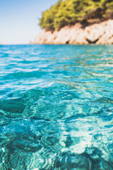 Foreground transparent clear sea water of azure color against the background of a distant rock