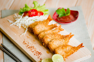 Butterfly ebi furai shrimp served with tomato and lettuce on a wooden chopping board along with ketchup