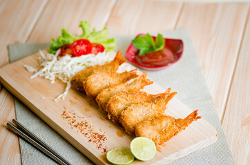 Butterfly ebi furai shrimp served with tomato and lettuce on a wooden chopping board along with ketchup