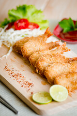 Butterfly ebi furai shrimp served with tomato and lettuce on a wooden chopping board along with ketchup