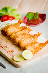 Butterfly ebi furai shrimp served with tomato and lettuce on a wooden chopping board along with ketchup