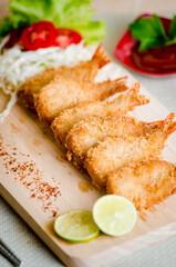 Butterfly ebi furai shrimp served with tomato and lettuce on a wooden chopping board along with ketchup