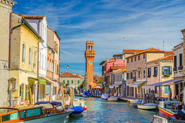 Murano islands with clock tower Torre dell'Orologio, boats and motor boats in water canal, colorful traditional buildings, Venetian Lagoon, Veneto Region, Northern Italy. Murano postcard cityscape. - obrazy, fototapety, plakaty