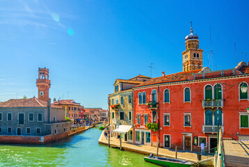 Fototapeta na wymiar Murano islands with bridge across water canal, boats and motor boats, colorful traditional buildings, clock tower Torre dell'Orologio, Veneto Region, Northern Italy. Murano postcard cityscape.
