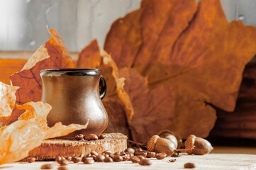 Background with autumn mood in brown. the cup stands among dry brown leaves, acorns, and a round glass jar with cookies stands in the back.