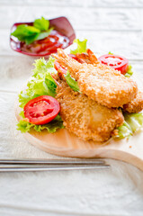 Butterfly ebi furai shrimp served with tomato and lettuce on a wooden chopping board along with ketchup
