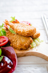 Butterfly ebi furai shrimp served with tomato and lettuce on a wooden chopping board along with ketchup
