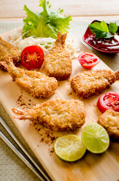 Butterfly ebi furai shrimp served with tomato and lettuce on a wooden chopping board along with ketchup