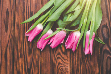 Bouquet of pink tulips on brown wooden background.
