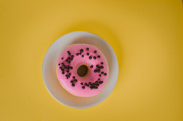 Pink round donut at bright yellow background with coffee glass
