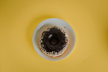 Black round donut at bright yellow background with coffee glass
