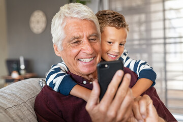 Child hugging grandpa while using smartphone