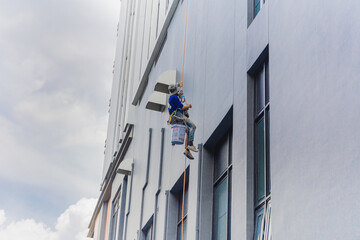 Painter coming down the facade of a building tower rappelling with a rope.