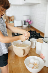 Fototapeta na wymiar Child girl preparing dough for pancakes at the kitchen. Casual lifestyle photo series in real life interior