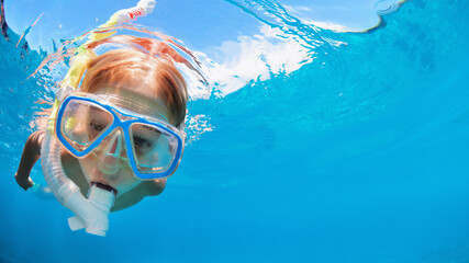 Happy little kid in snorkeling mask and wetsuit jump and dive underwater in coral reef sea lagoon....