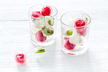 Cocktail glasses with berries in ice cubes on white table