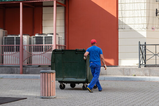 Gorki Gorod, Sochi, Russia, July, 9, 2020: a male cleaner in a blue uniform and red cap cleans garbage on the streets of the city
