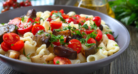 Pasta creste with grilled eggplant, cherry tomatoes and herbs. Delicious warm salad. Close up