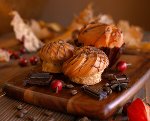 A couple of delicious eclairs and a muffin on a wooden table with autumn decoration 