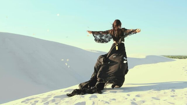 woman in a black dress. hands raised to the sky throws, sprinkles gold sequins