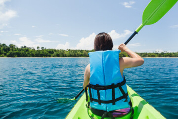 Woman with lifejacket kayaking in tropical island ocean on vacation.