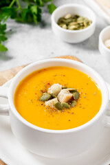 Pumpkin soup. Pumpkin cream soup in a white plate on the light gray kitchen table. Vegetarian autumn soup closeup	