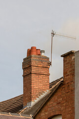 Red brick chimney stack with clay pots and TV aerial on English tiled rooftop