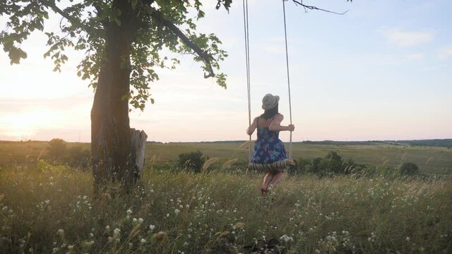 Young girl swinging on a swing under a tree in sun. Family fun in nature.