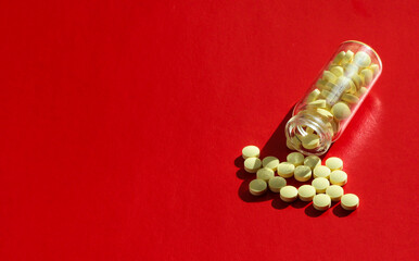 A bottle of yellow pills. Tablets are scattered on a red background.