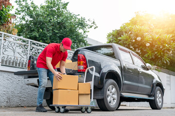 Delivery men in red uniform unloading cardboard boxes from pickup truck. Courier man sending the parcel or package to the customer on a business day. Online shopping and transport logistics concept. - obrazy, fototapety, plakaty