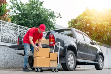 Deurstickers Delivery men in red uniform unloading cardboard boxes from pickup truck. Courier man sending the parcel or package to the customer on a business day. Online shopping and transport logistics concept. © godji10
