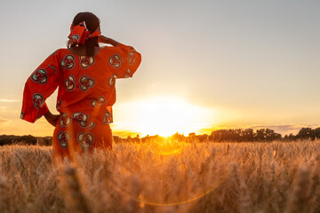African woman in traditional clothes standing in a field of crops at sunset or sunrise - 377859066