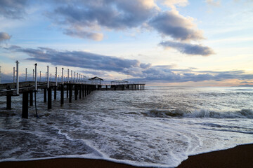 View from beach to water of sea, waves with white foam, pierce and sky with clouds in a nice evening.