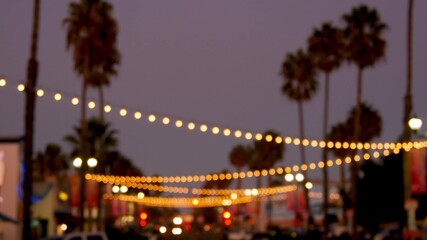 Fototapeta na wymiar Decorative staring garland lights, palm trees silhouettes, evening sky. Blurred Background. Street decorated with lamps in California. Festive illuminations, beach party, tropical vacations concept.
