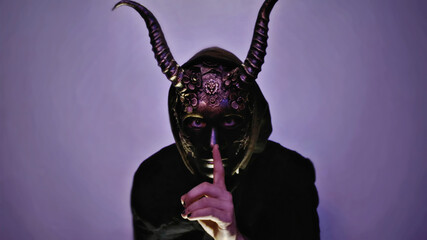 a person wearing a horned mask isolated on a purple lit background.