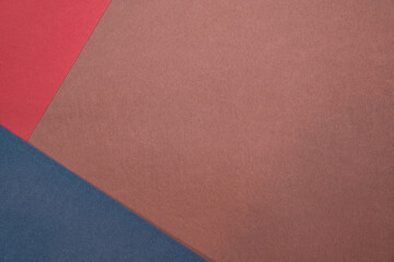 Fototapeta premium Three sheets of colored paper on a brown background. Red, blue. Minimalistic composition. Background for text or design. Empty right side. Top view