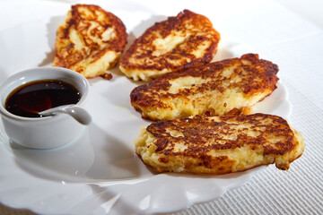 Pancakes on white plate and sweet liquid honey or caramel with a small spoon and with background. Delicious fried flour food. Unhealthy and harmful, but very tasty food.