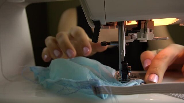 Close-up female hands sew a protective mask.Making a homemade face mask on a sewing machine.